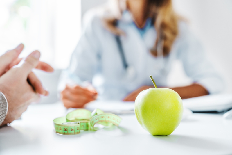 bluured pharmacist in background focused on a green apple and measuring tape