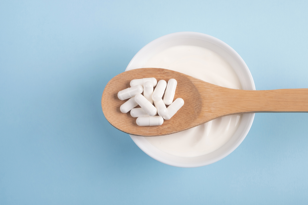 probiotic supplement capsules on wooden spoon over bowl of yogurt