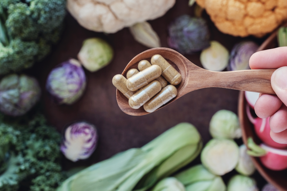 hand holding wooden spoon with fiber capsules over assortment of vegetables