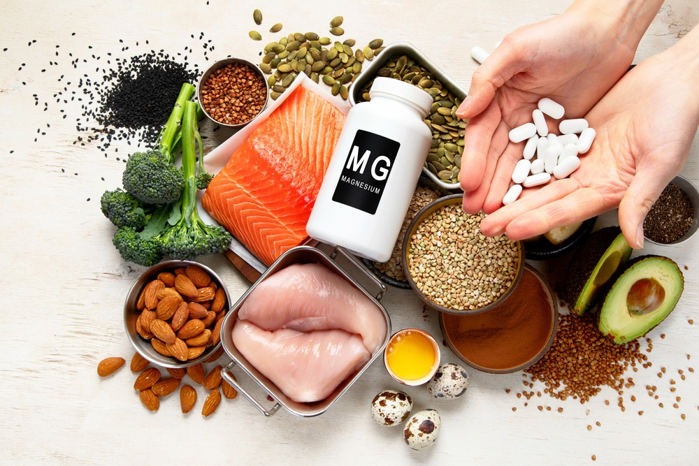 hands holding white magnesium supplements over assorted magnesium-rich foods