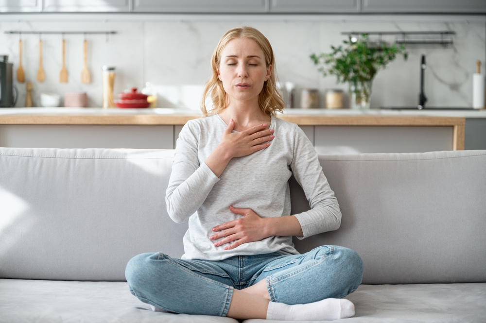 woman sitting cross-legged on couch doing breathing exercises to reduce stress